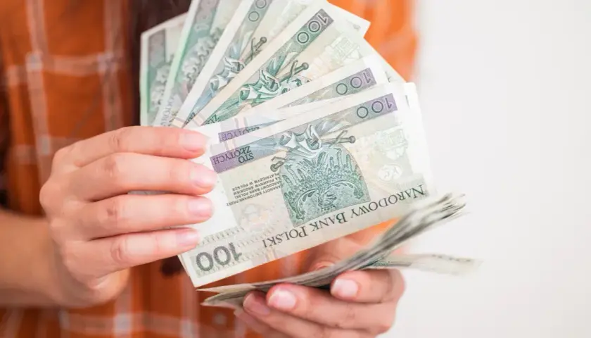 Ręce trzymające stos banknotów 100 zł. Zastanawiasz się, ile wynosi zasiłek dla bezrobotnych?