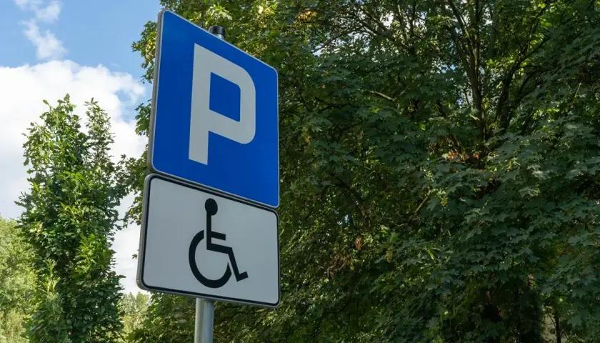 Niebieski znak "P" i biały znak z symbolem wózka inwalidzkiego. To miejsce parkingowe dla osób z niepełnosprawnościami, które posiadają odpowiednią kartę parkingową.