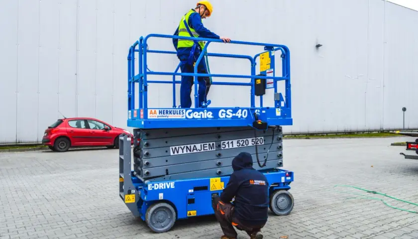 Dwóch pracowników w kaskach i kamizelkach na podnośniku koszowym Genie GS-40.