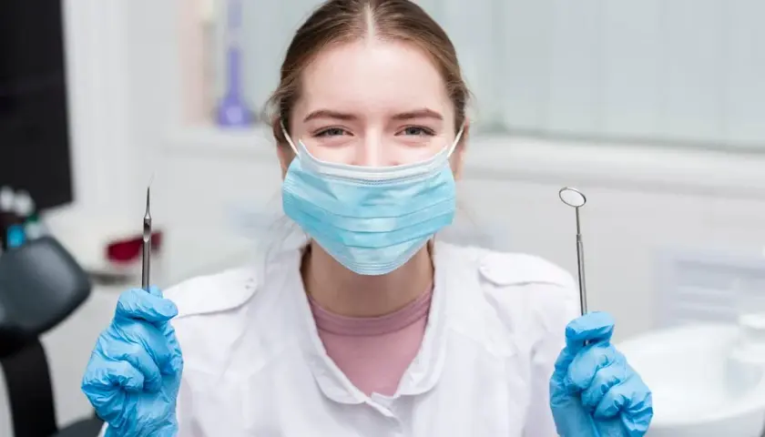 Uśmiechnięta asystentka stomatologiczna w maseczce i rękawiczkach trzyma narzędzia. Czas na egzamin!