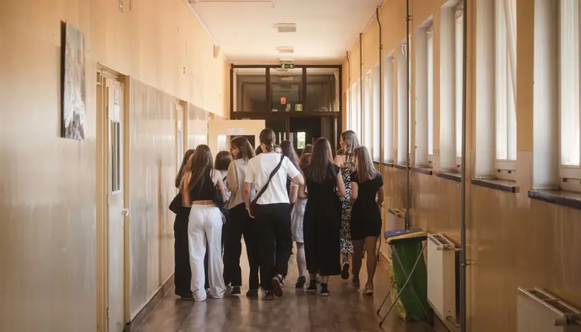 Grupa uczniów w szkolnym korytarzu, nerwowo oczekująca na rozpoczęcie egzaminów ósmoklasisty.