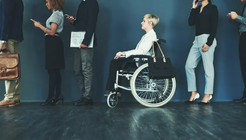 Różne rodzaje niepełnosprawności w kolejce do pracy: osoba na wózku inwalidzkim i inni kandydaci.