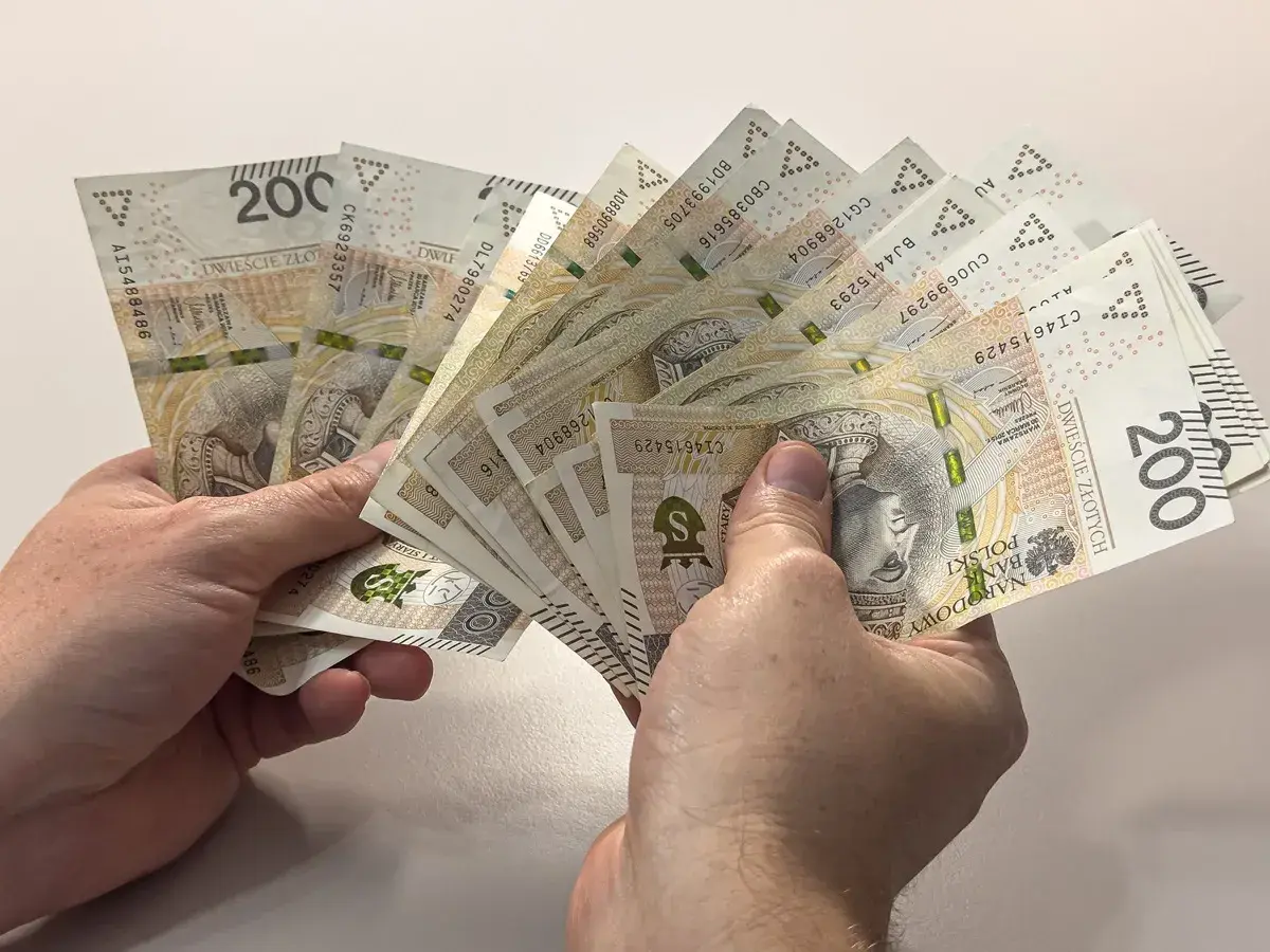 Ręce trzymające plik banknotów 200 zł. Dyskusja na forum: przeliczenie emerytury po 65 roku życia.