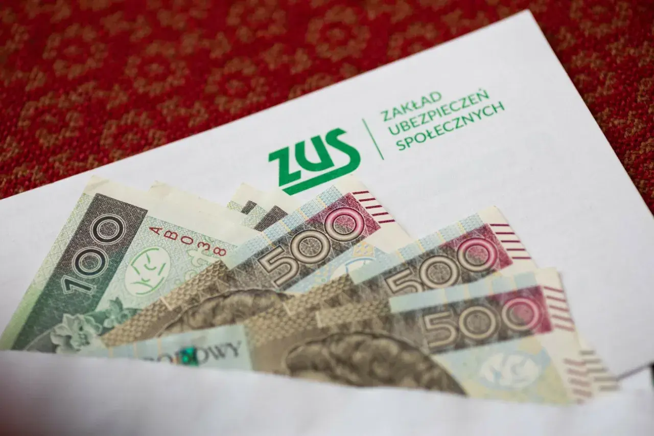 ZUS odszkodowania cennik tabela: banknoty 100 i 500 zł w kopercie z logo ZUS.