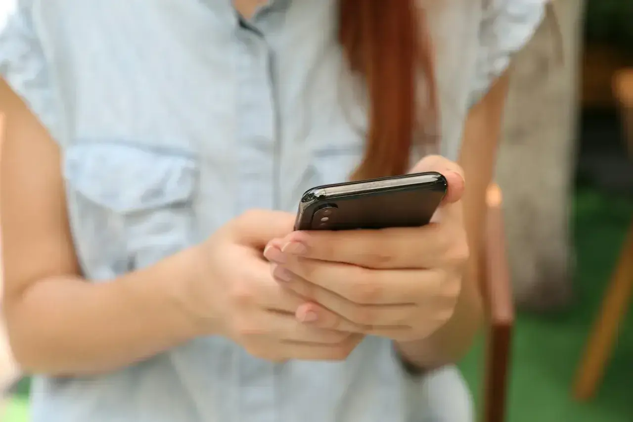 Kobieta w jasnej koszuli trzyma smartfon, szukając informacji, gdzie sprawdzić L4.