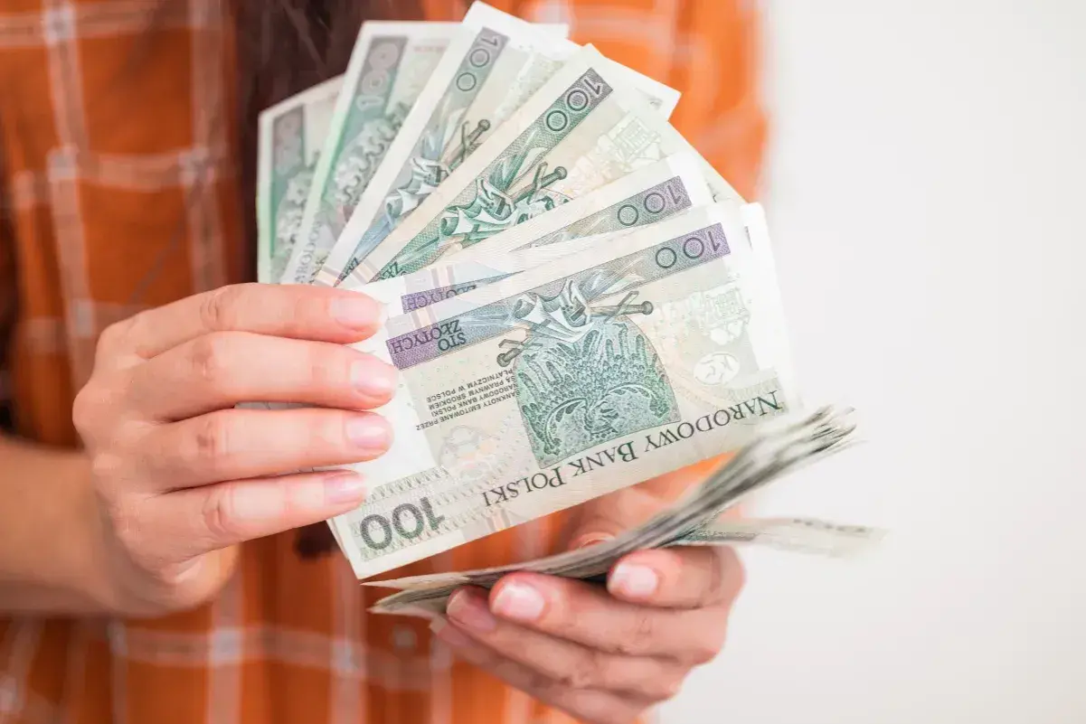 Ręce trzymające stos banknotów 100 zł. Zastanawiasz się, ile wynosi zasiłek dla bezrobotnych?