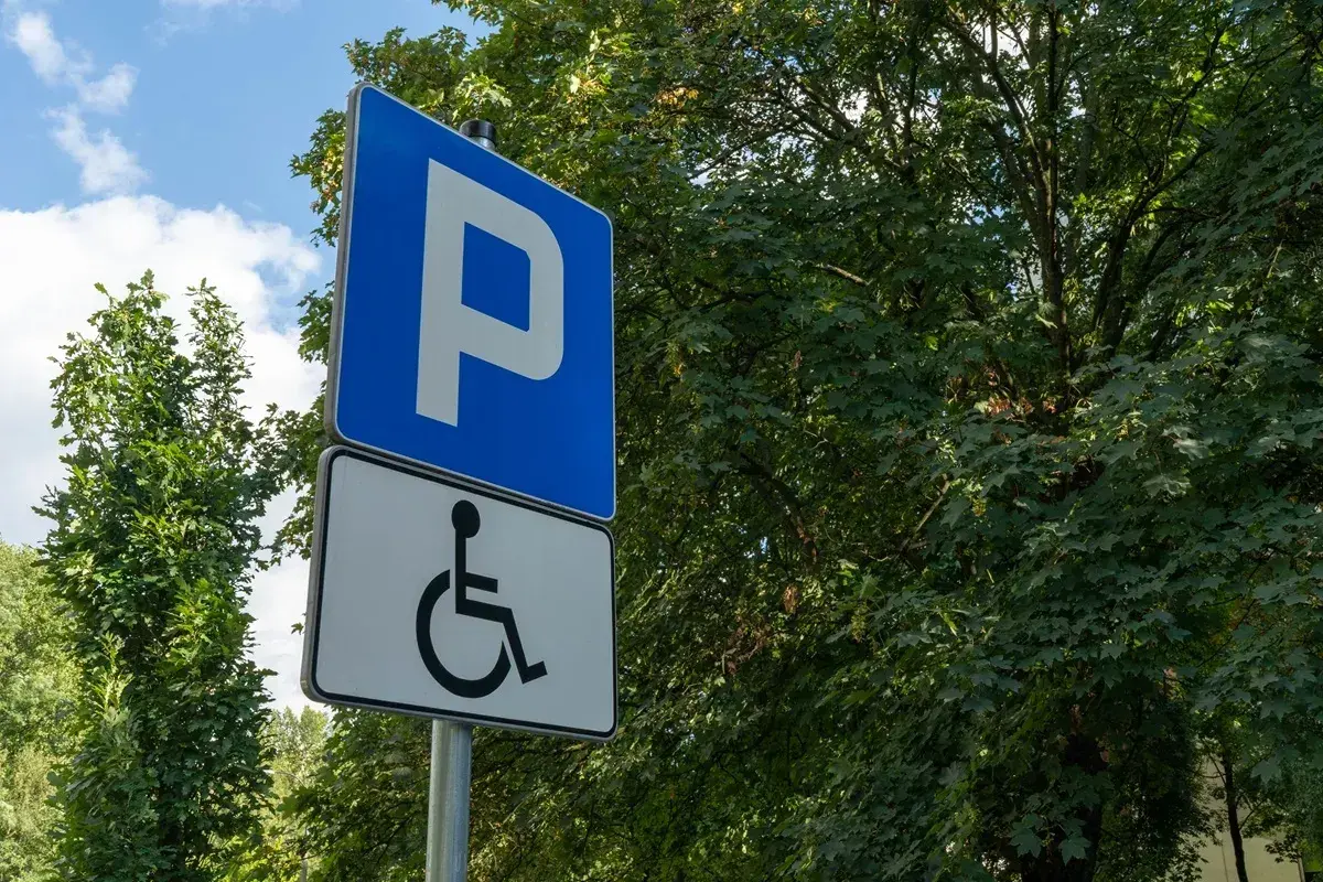 Niebieski znak "P" i biały znak z symbolem wózka inwalidzkiego. To miejsce parkingowe dla osób z niepełnosprawnościami, które posiadają odpowiednią kartę parkingową.