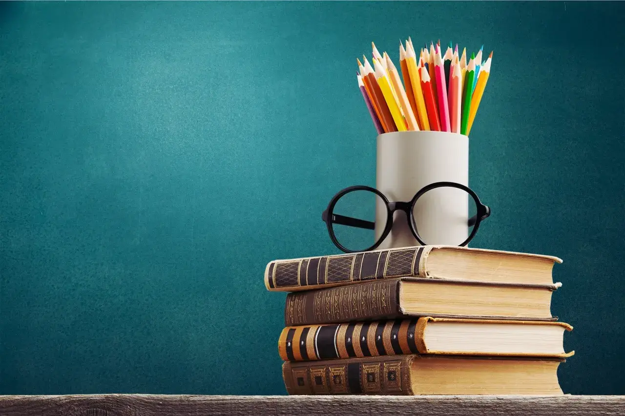 Stos książek, okulary i kredki na tle tablicy. To symbol wiedzy, która otwiera drzwi do kariery, nawet jeśli to co to znaczy wykształcenie średnie branżowe.