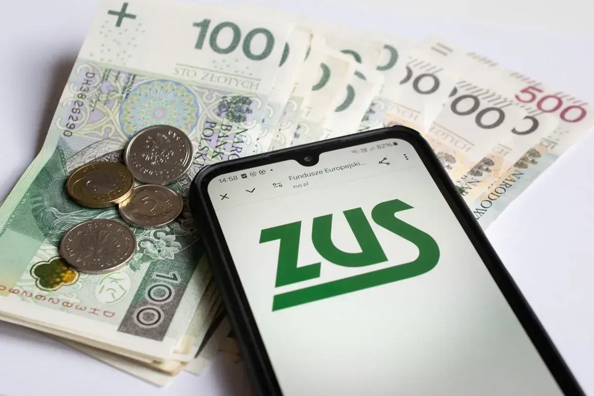 Złotówki i monety obok telefonu z logo ZUS. Sprawdzasz, czy zasiłek pogrzebowy 6000 zł wystarczy na pokrycie kosztów.