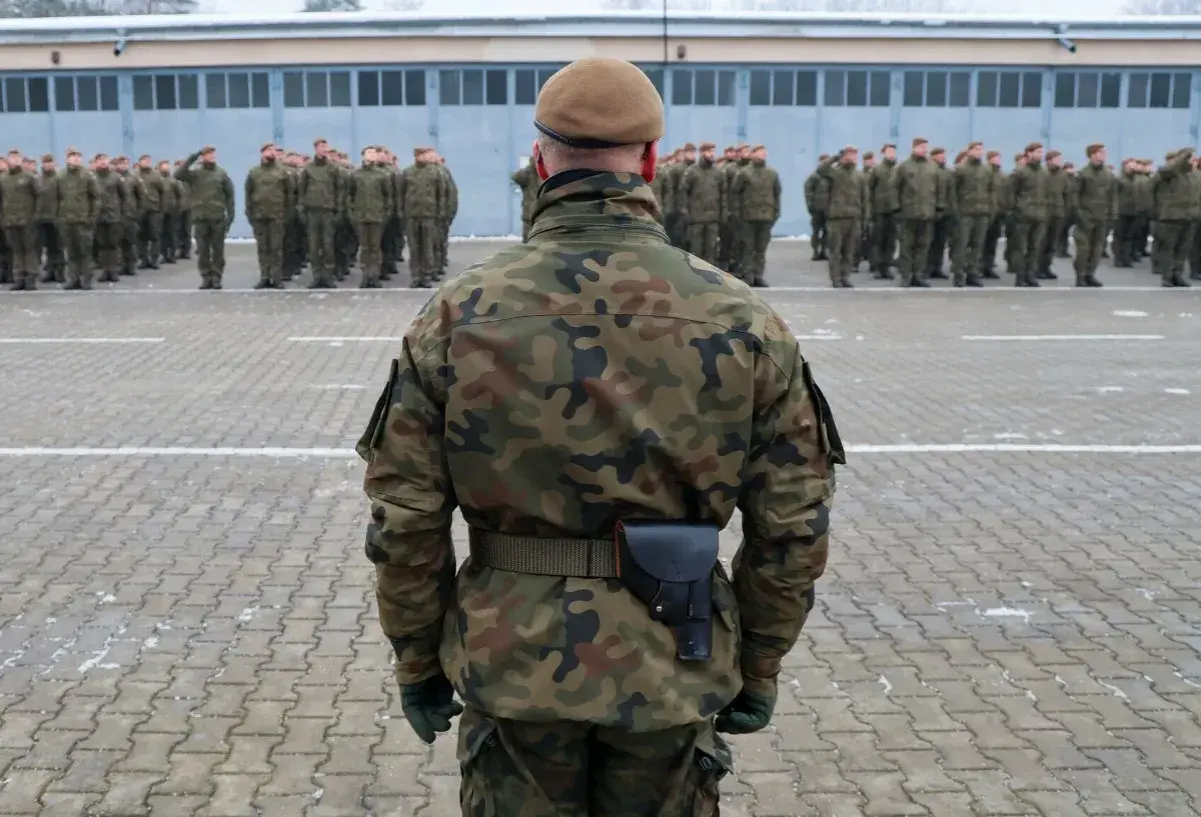Żołnierz w mundurze polowym stoi na placu apelowym przed szeregiem innych żołnierzy. Czy w wieku 35 lat można iść do wojska? Tak, wiek nie jest przeszkodą.