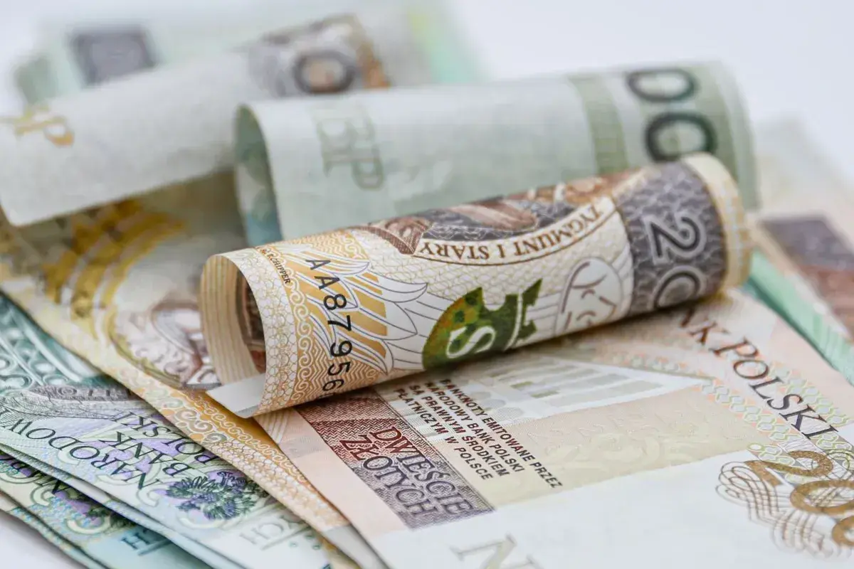 Zwijane polskie banknoty, w tym 20 złotych, symbolizują oszczędności na dodatkowy urlop.