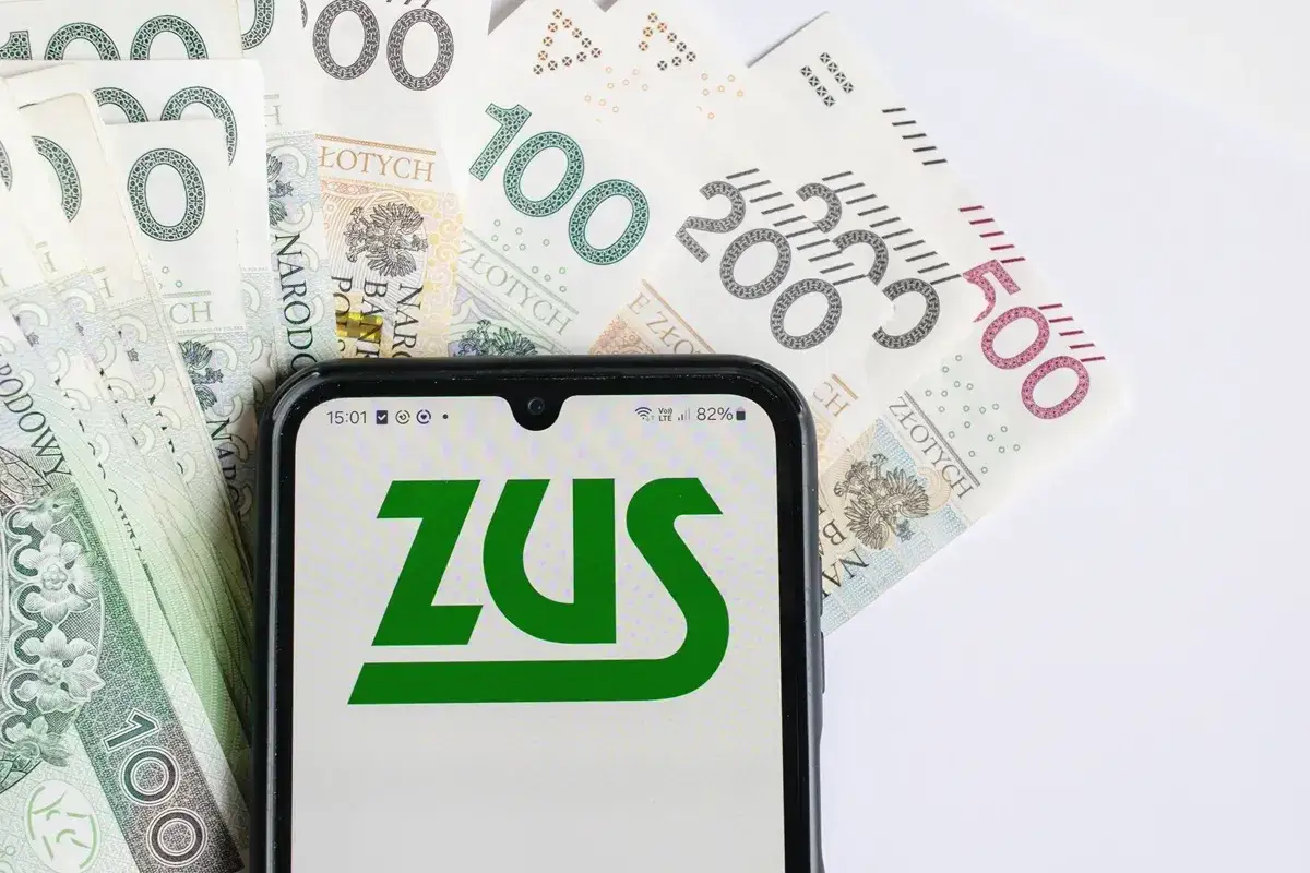 Telefon z logo ZUS na tle polskich banknotów. Informacje o 13 emeryturze 2026 - tabela.