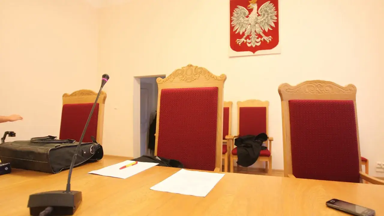 Sądowa sala z godłem Polski. Zastanawiasz się, ile zarabia sędzia? Na stole mikrofon, dokumenty i torba.