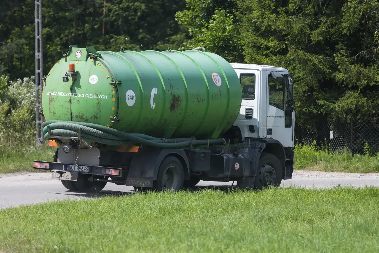 Zielona beczka na śmieci na białej ciężarówce. Ten szambonurek jest gotowy do pracy, wywożąc nieczystości ciekłe.