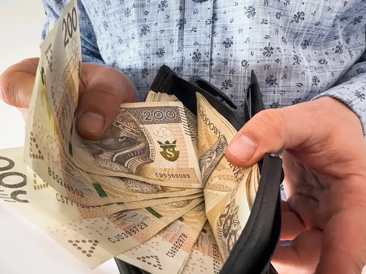 Ręce trzymają portfel z banknotami 200 zł. To może być nagroda jubileuszowa, która cieszy.