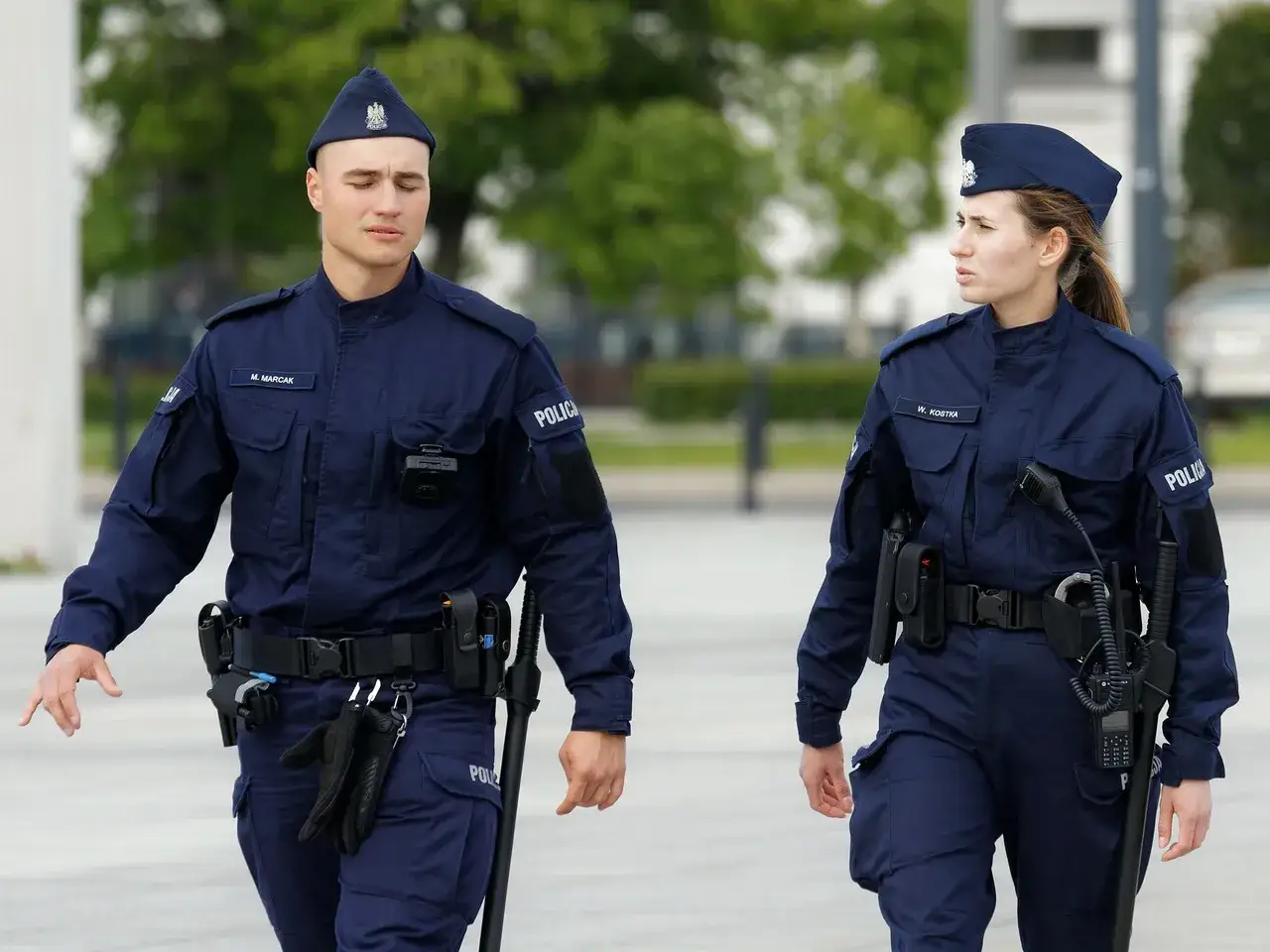 Dwóch policjantów w mundurach, dyskutujących o zarobkach w policji.